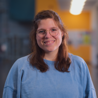 Foto von Amelie Unger - weiblich, braune offene Haare und Brille mit einem blauen Oberteil vor einem verschwommenen Hintergrund.
